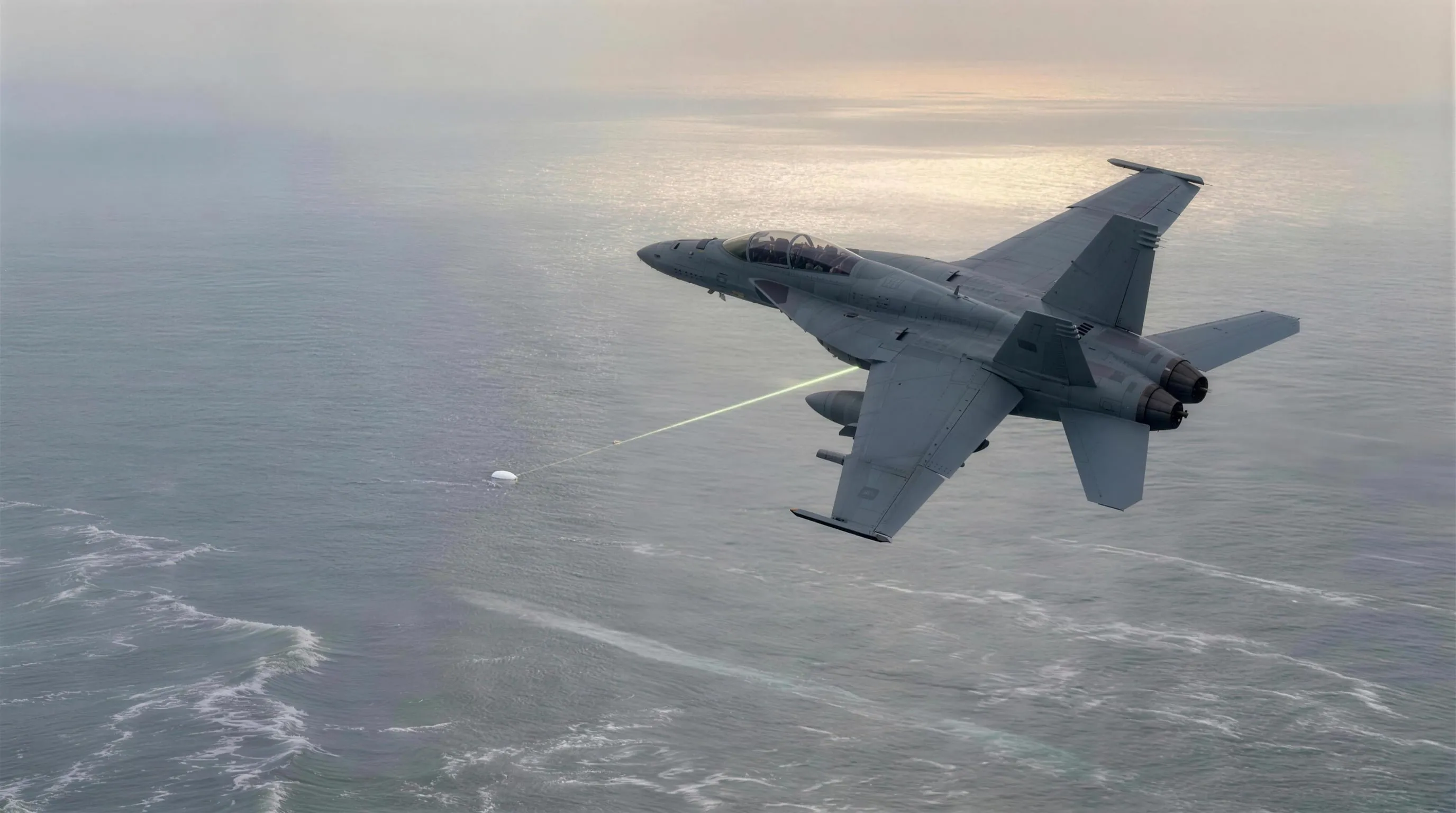 A grey F/A-18 Super Hornet banking over a hazy silver Atlantic in low afternoon light, a thin luminous sensor line reaching down from its targeting pod toward a tiny white oval object far below, with a faint ghostly streak racing along the wave tops in the distance beneath it.
